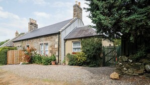 A stone house with a gravel driveway, a wooden fence, and a stone wall. - Katmoget Cottage (Cupar)