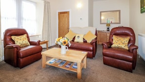 A cozy living room with leather armchairs, a wooden coffee table with magazines, and a floral arrangement. - Katmoget Cottage (Cupar)