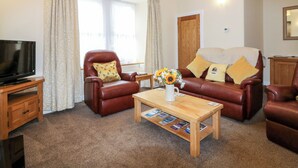 A living room with a television, leather armchairs, a wooden coffee table, and a bookshelf. - Katmoget Cottage (Cupar)