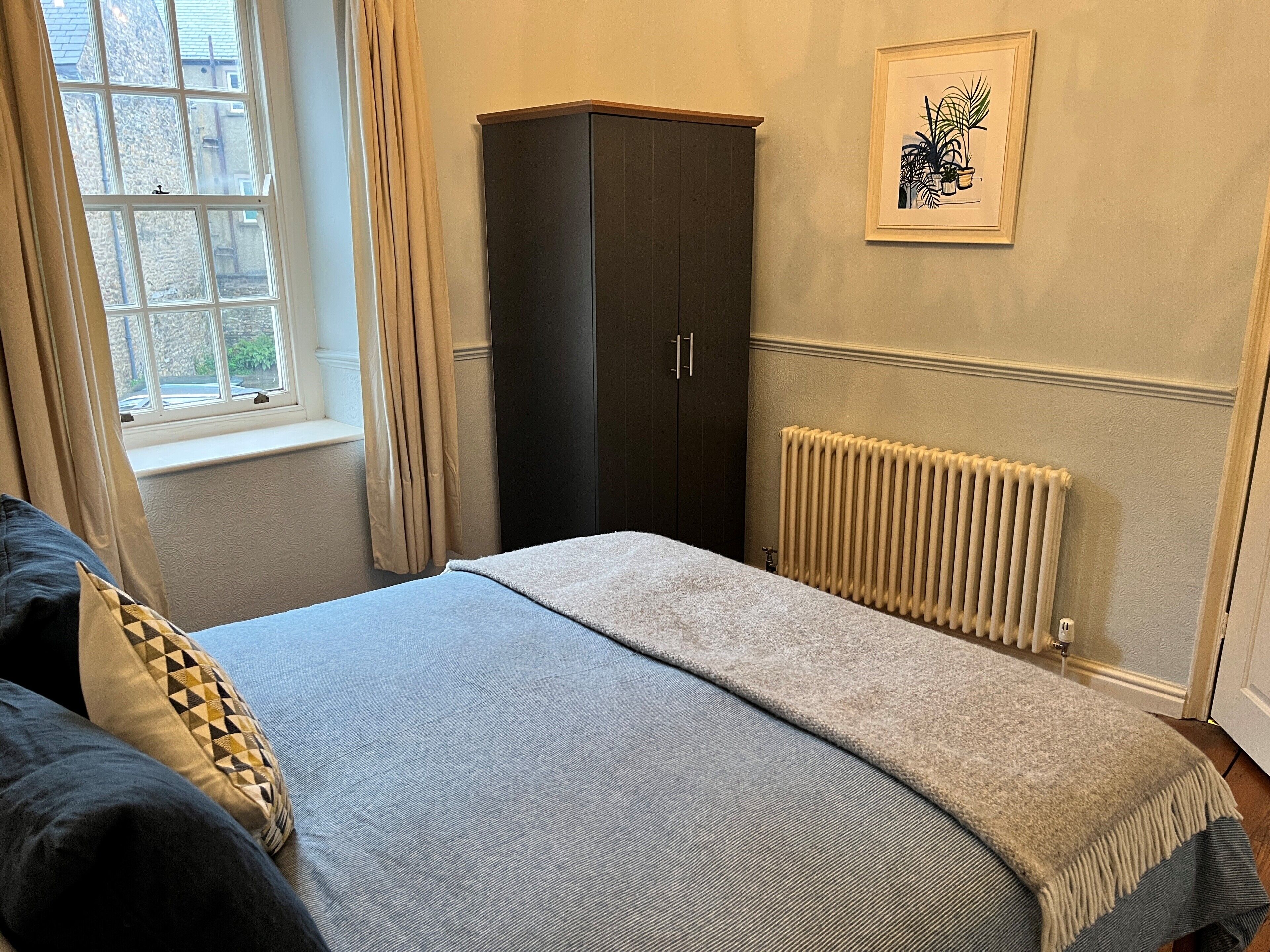 A bedroom with a bed, a wardrobe, a radiator, and a window with curtains.