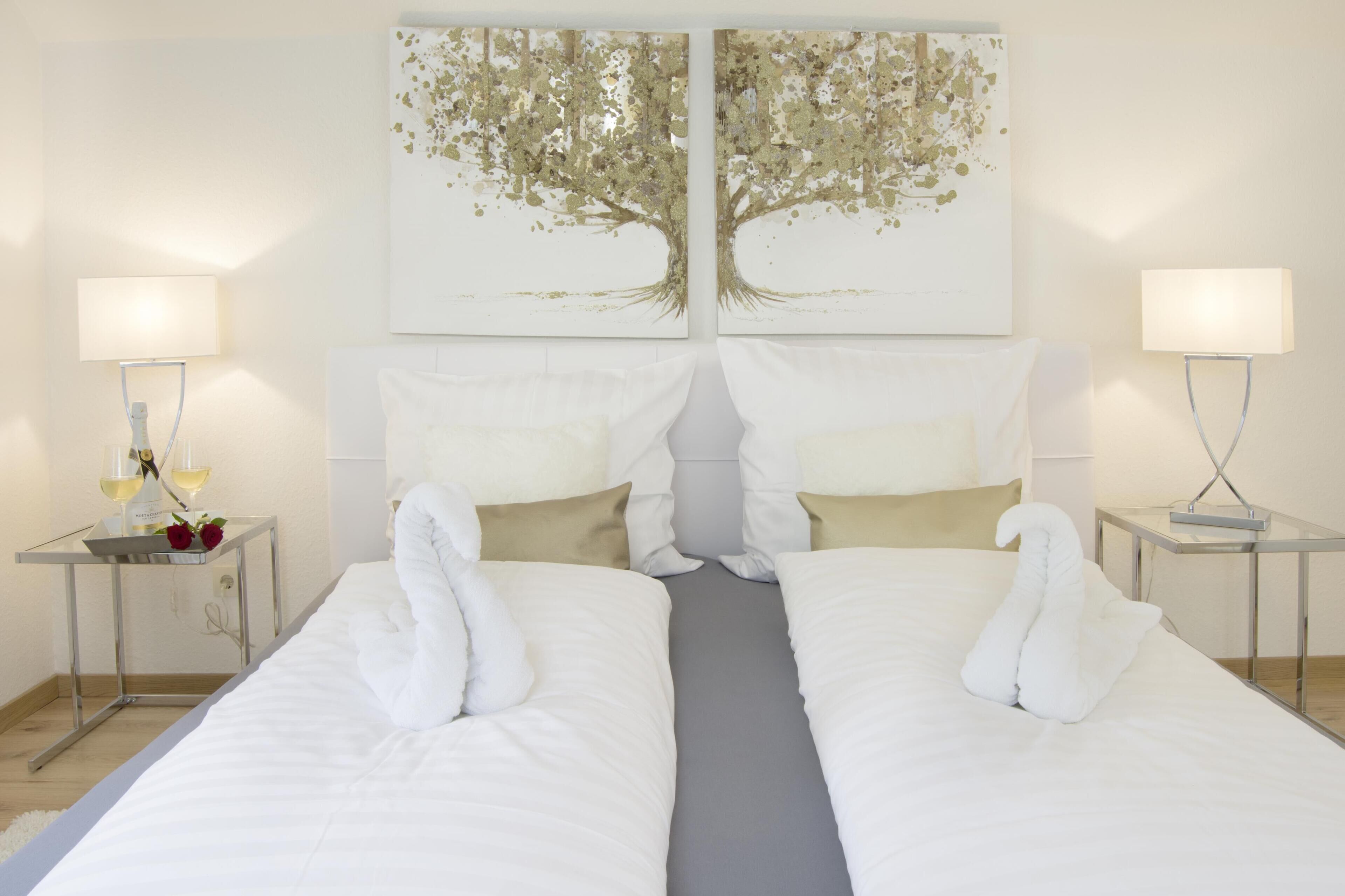 Una camera d'albergo con due letti, un quadro a tema alberi sopra e lampade ai comodini.