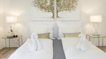 Una camera d'albergo con due letti, un quadro a tema alberi sopra e lampade ai comodini.
