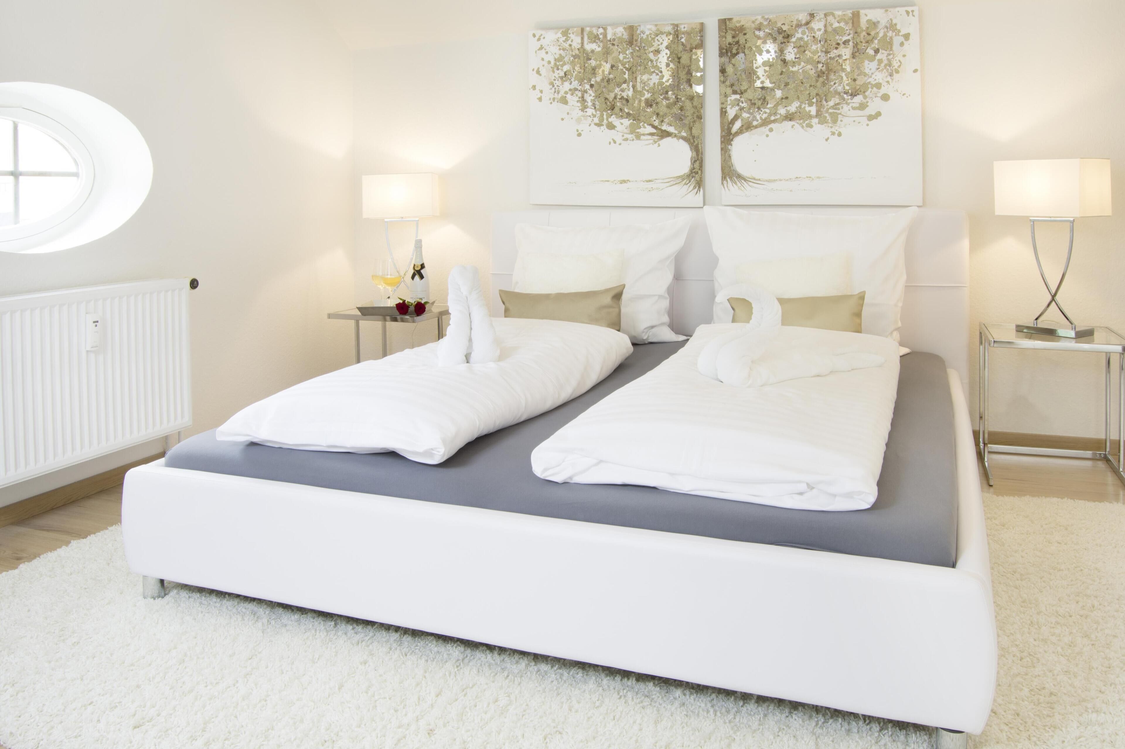Een moderne slaapkamer met een groot bed, twee nachtkastjes, een rond raam en wanddecoratie.