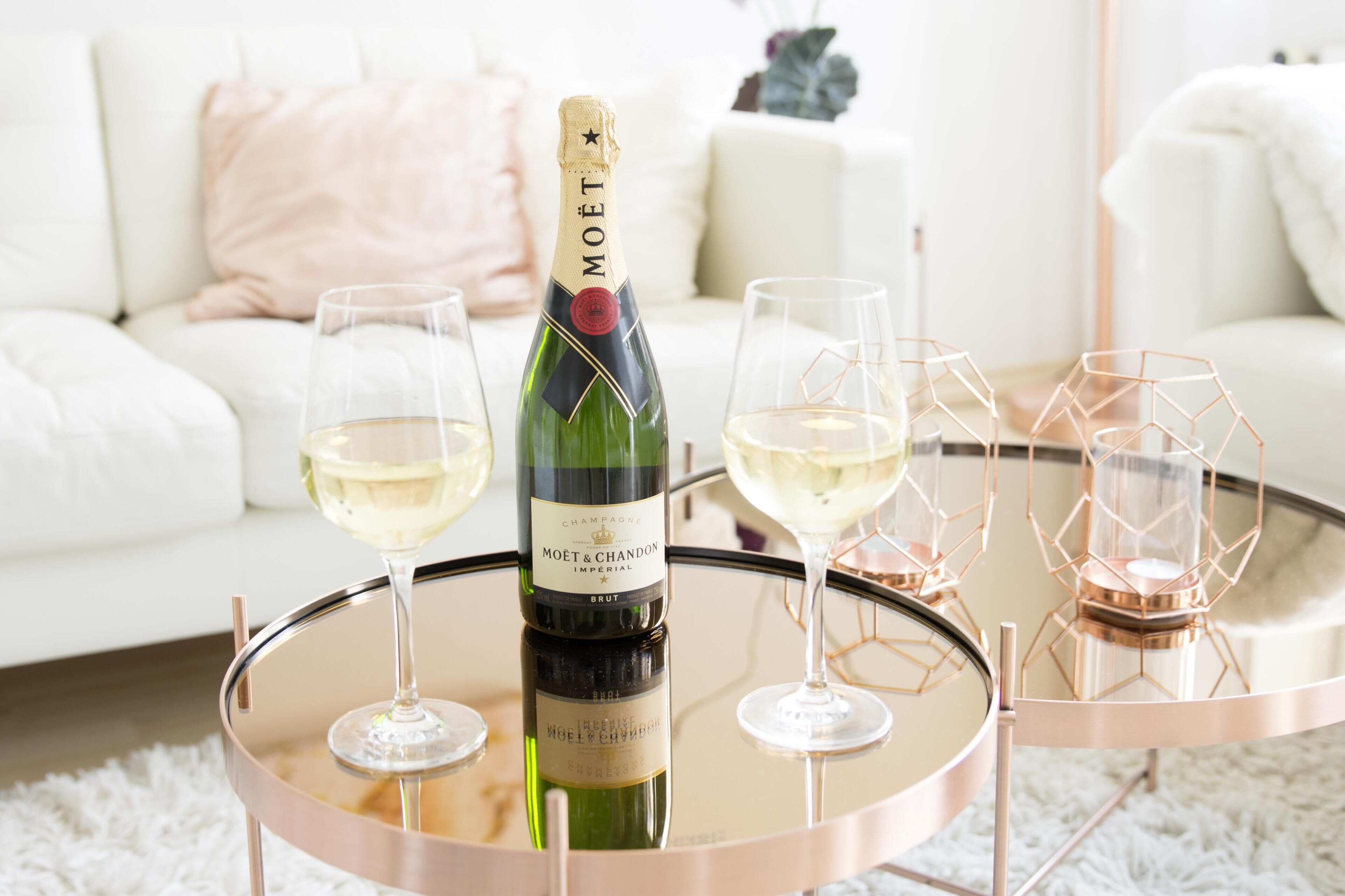 A bottle of Moët champagne on a glass table with three glasses of champagne.