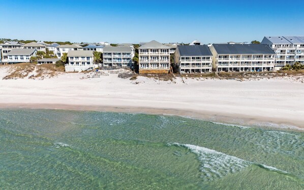 A beachfront hotel with multiple floors, balconies, and a sandy beach in the foreground.
