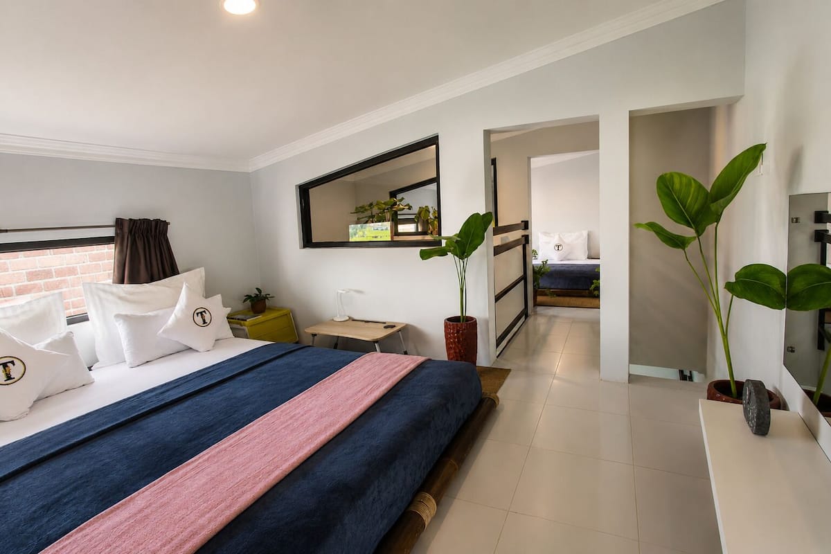 A modern hotel room with a large bed, a desk, a mirror, and potted plants.