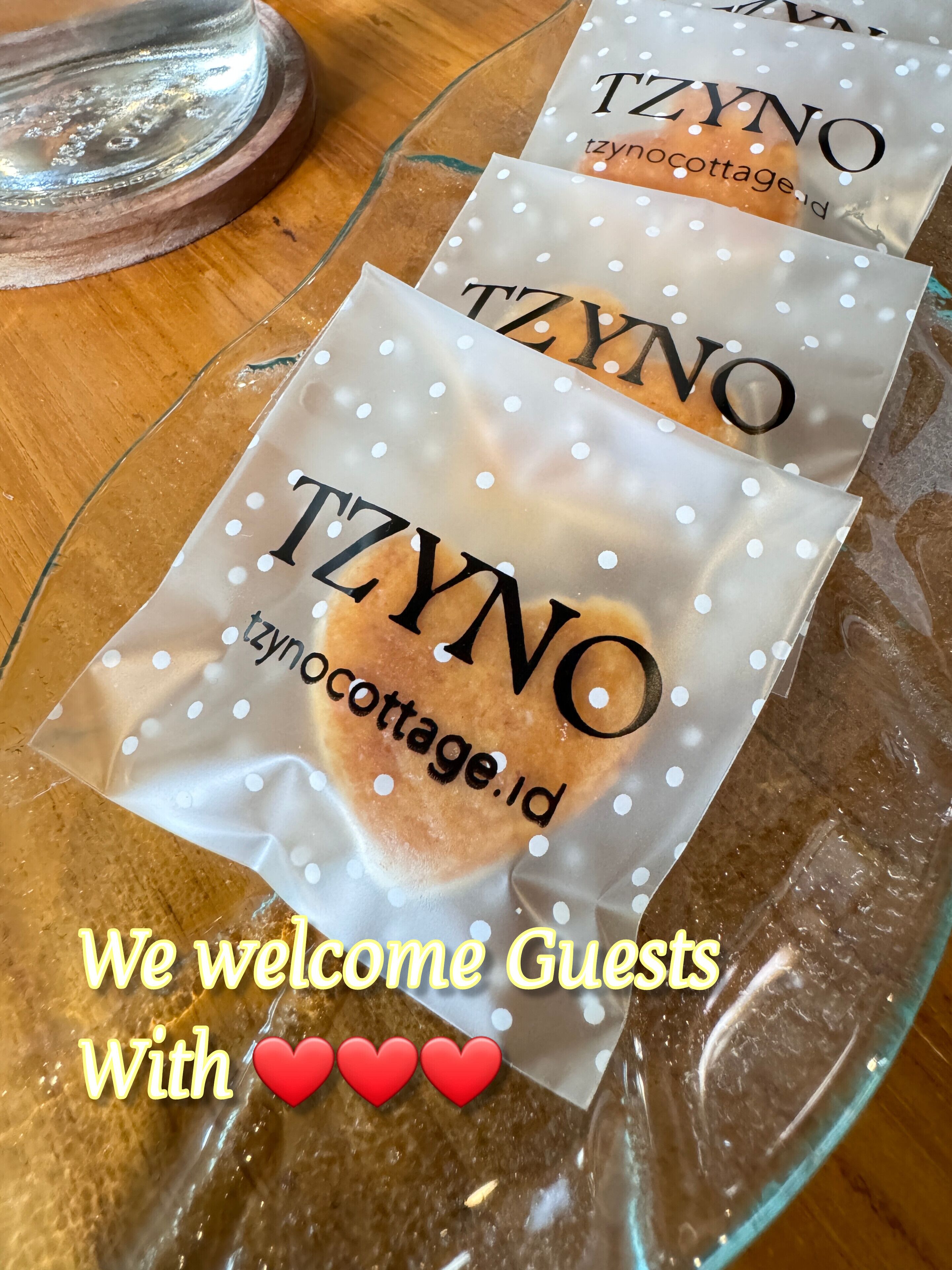 Deux sacs de marque portant les inscriptions « TZYNO » et « tzynocottage.id » sont posés sur une table en verre.