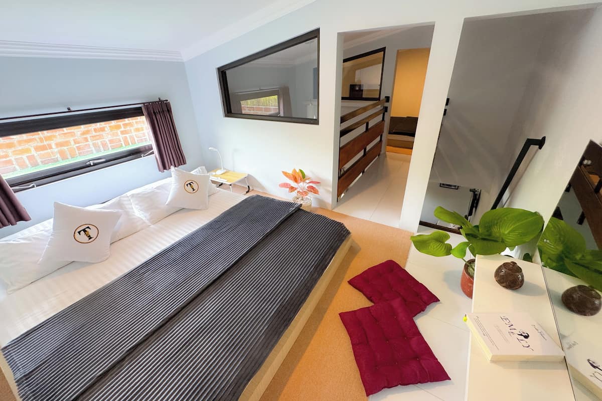 A modern hotel room with a large bed, a desk, a mirror, and a view of the outside.