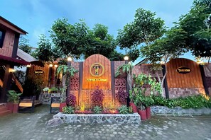 A wooden sign with "TZY-NO Cottage" written on it, surrounded by greenery and potted plants.