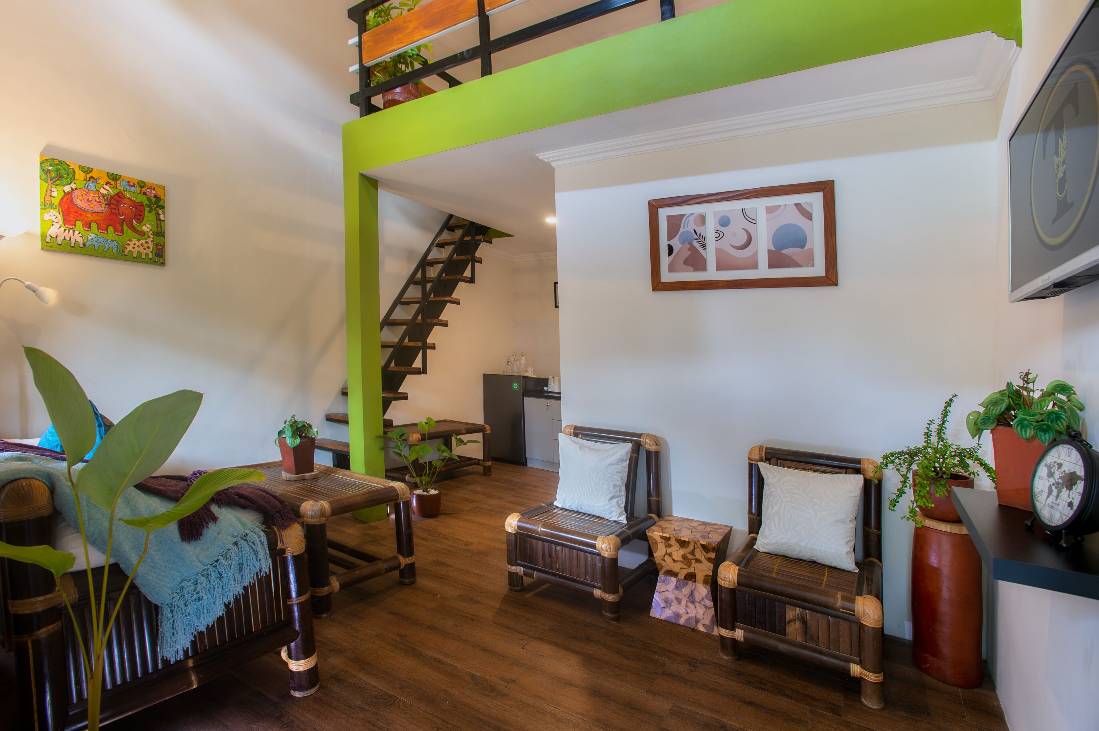 A room with a wooden floor, two wooden sofas, a small table, a staircase, and a green wall.