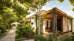 Un resort con una zona de estar al aire libre techada, un camino bordeado de plantas y un edificio con fachada de madera.