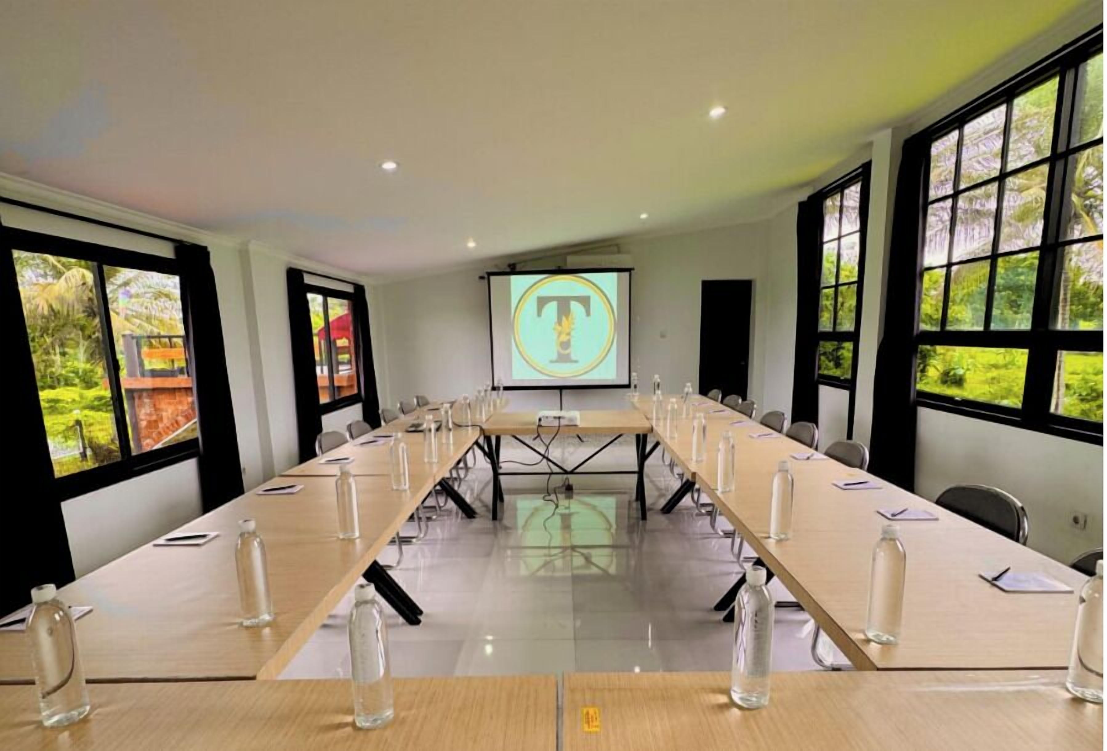 Une salle de conférence équipée d’une longue table, de chaises et d’un écran de projection affichant un logo.