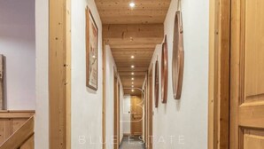 A long, narrow hallway with wooden floors and walls, featuring framed pictures on the walls and a wooden door at the end.