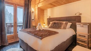 A bedroom with a wooden ceiling, a bed with a fluffy pillow, a small dog, and a suitcase on a dresser.
