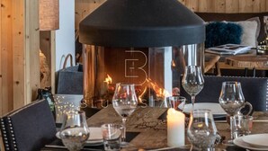 A cozy dining area with a wood-burning stove, a table set for a meal, and a view of a ski lift in the background.