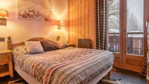 A cozy bedroom with a wooden bed, a nightstand, a wall-mounted lamp, and a window with curtains.