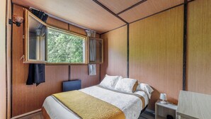 Un dormitorio con cama, mesita de noche, lámpara, ventana con cortinas y vista a zonas verdes.