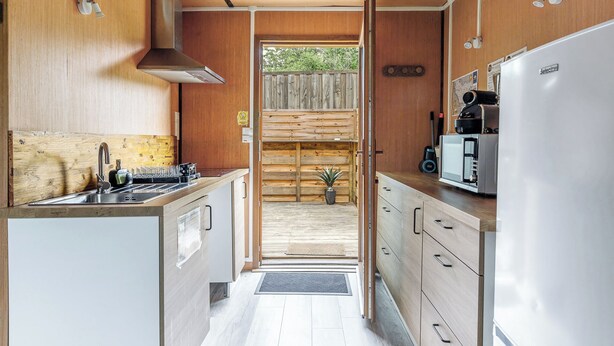 Una cocina compacta con paredes de madera, un lavamanos de acero inoxidable y una estufa empotrada.