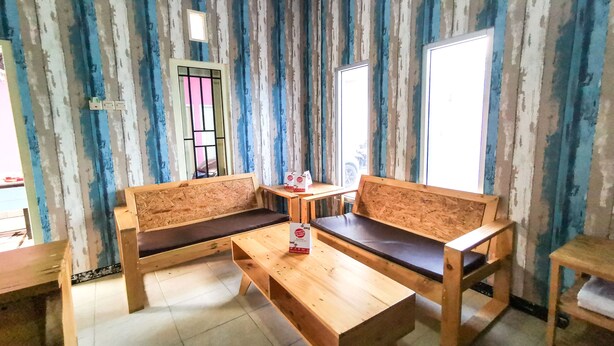 Une pièce avec un papier peint à rayures, deux bancs en bois avec des coussins, une petite table et une fenêtre avec une grille en métal.