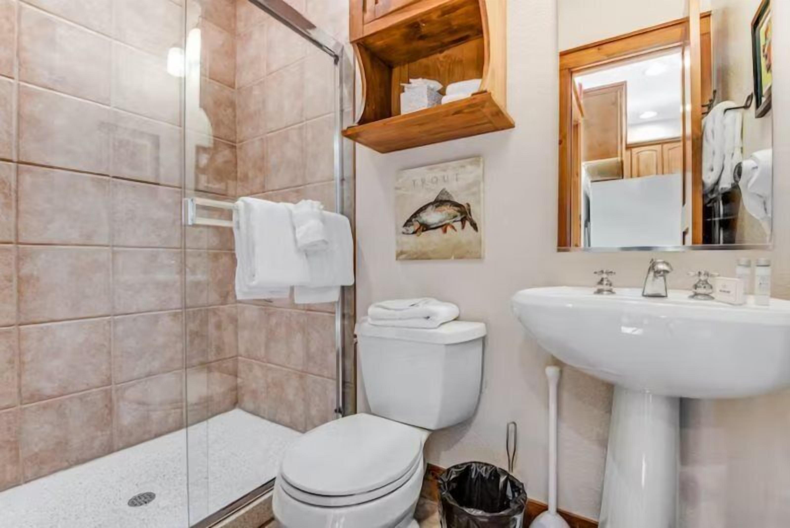 Une salle de bain avec une douche à parois de verre, des toilettes, un lavabo et une étagère en bois au-dessus du lavabo.