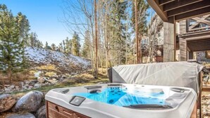 Ein Whirlpool mit Holzaußenverkleidung und weißem Deckel, eingebettet in eine natürliche Umgebung mit Bäumen und Felsen.