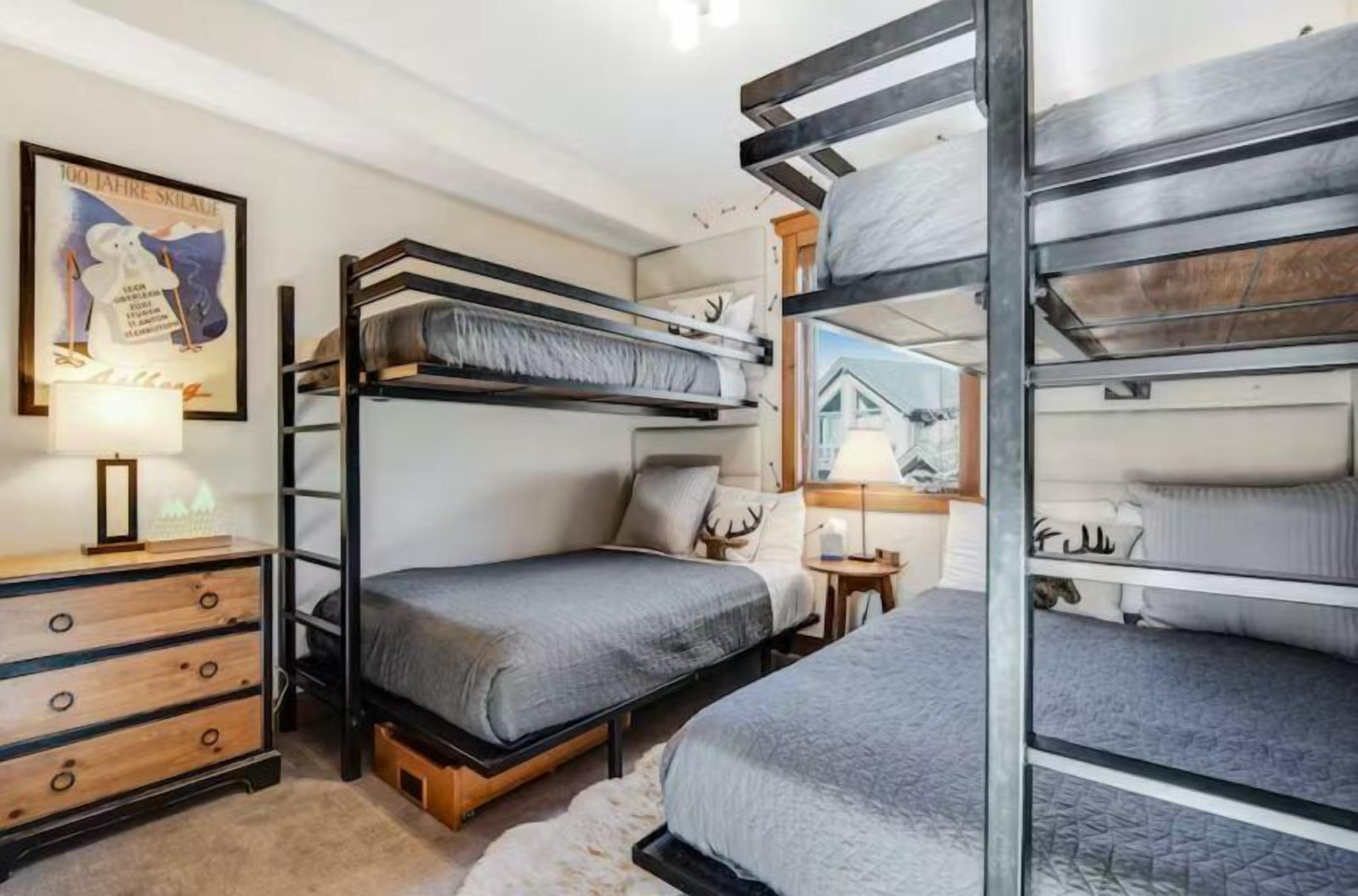 Una camera con letto a castello, una cassettiera in legno, un quadro incorniciato e un tavolino con una lampada.