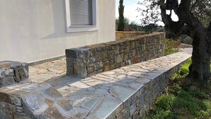 Un mur de soutènement en pierre, avec un chemin également en pierre menant à l’entrée d’un bâtiment.