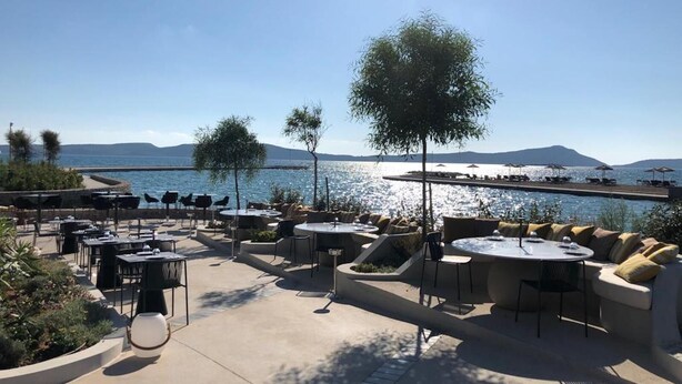 Un espace extérieur aménagé avec des tables et des chaises, offrant une vue sur une étendue d’eau et sur des montagnes lointaines.