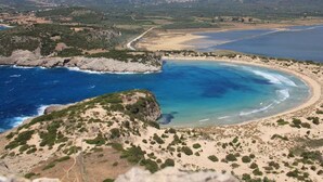 Un paysage côtier comprenant une plage, un terrain rocheux et des montagnes à l’horizon.