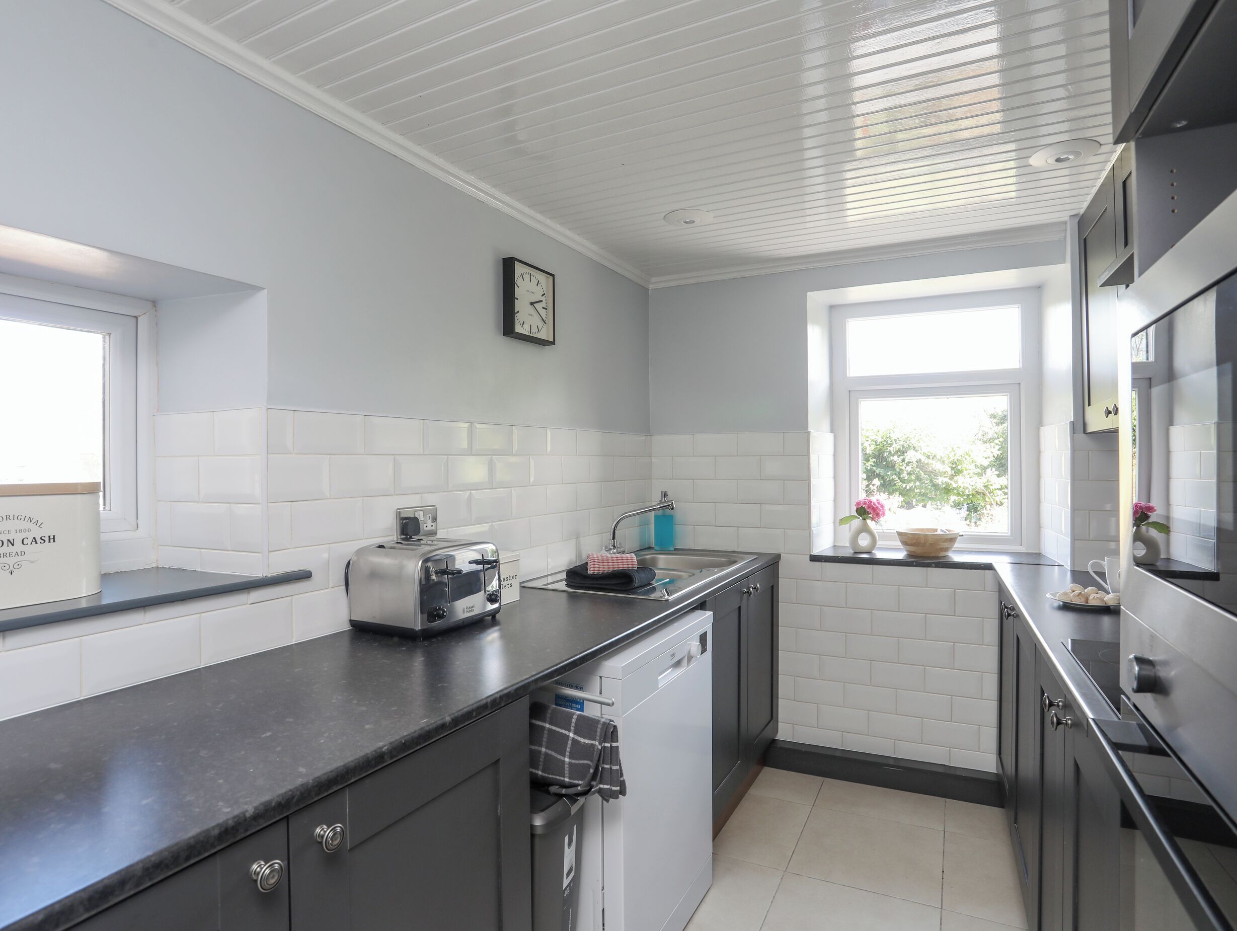 A modern kitchen with white subway tiles, a black countertop, a toaster, a sink, and a window with a view of greenery.