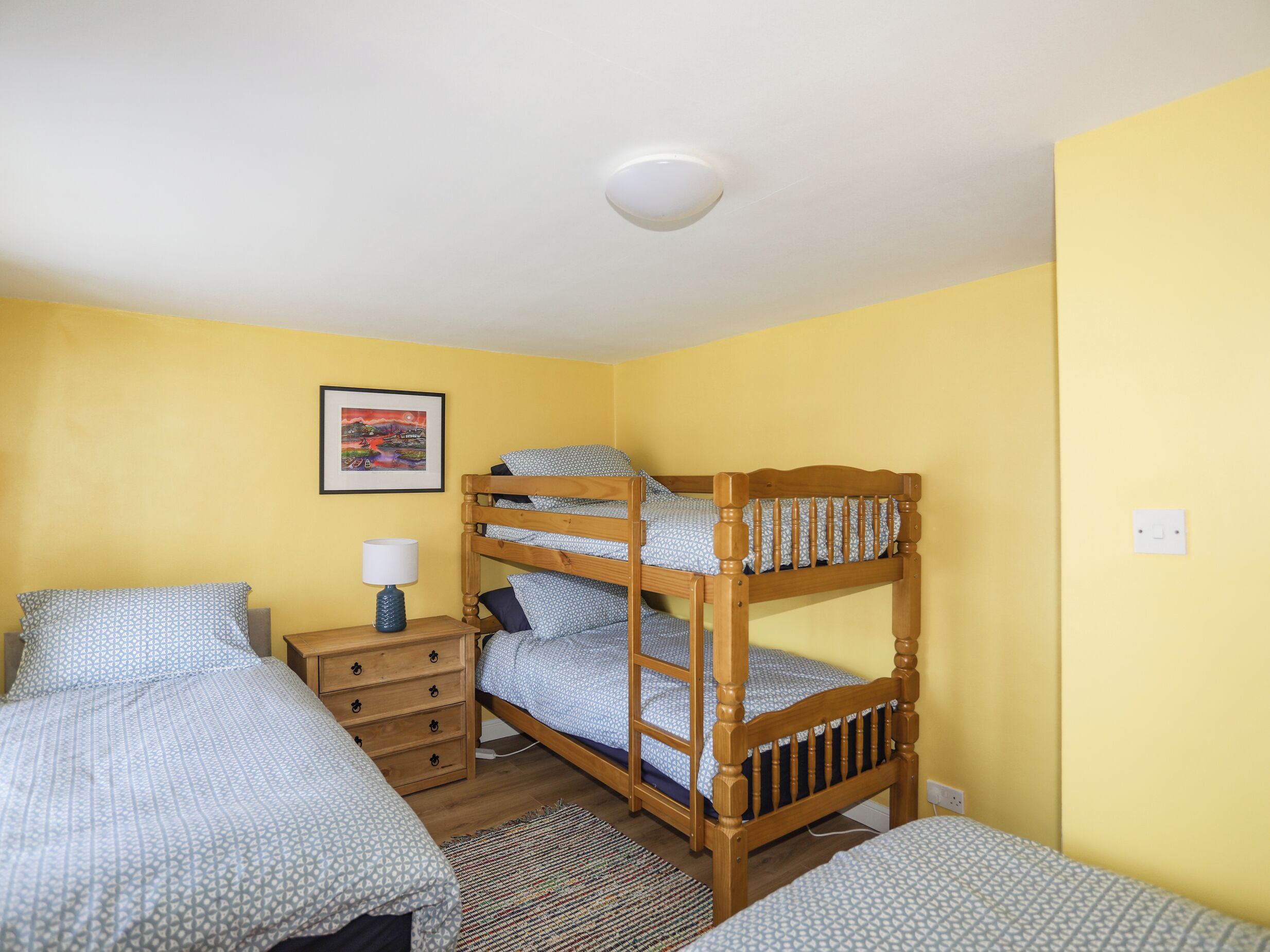 Een slaapzaal met stapelbedden, een houten dressoir, een bedlampje en een lijst met foto aan de muur.