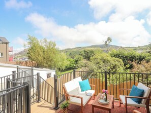 A balcony with white sofas, a wooden table, and a metal railing. - Maes Y Ffynnon (Pwllheli)
