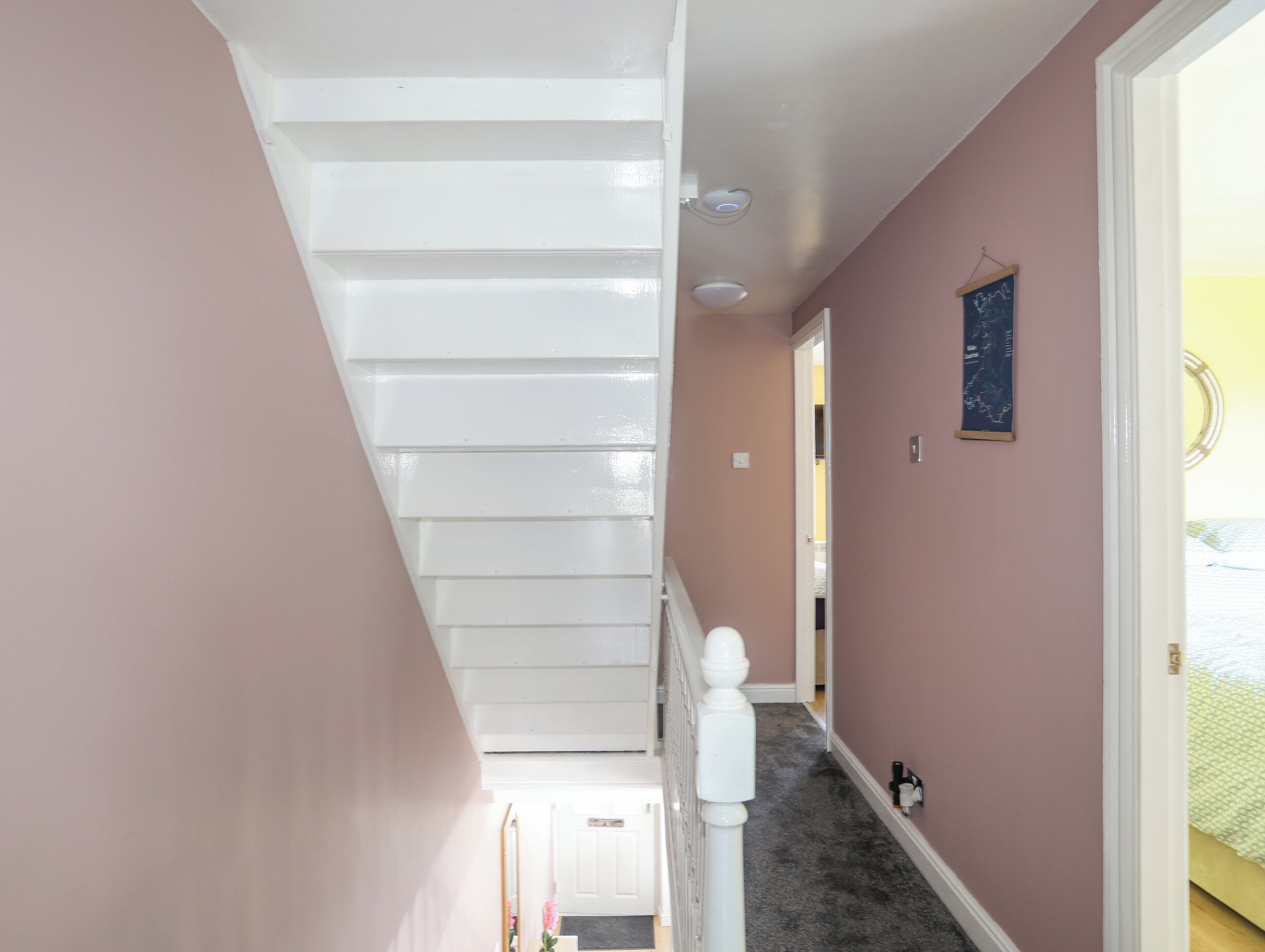A staircase with white railings and a carpeted hallway with pink walls.