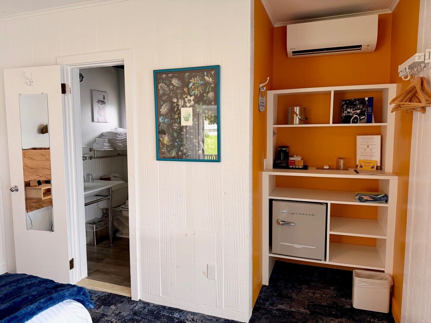 A room with a bed, a wardrobe, a shelf with items, and a door leading to another room.