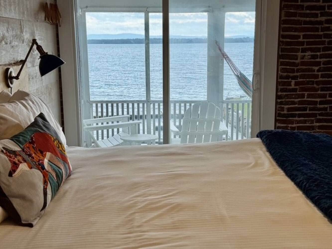Una cama con vista al agua, una silla blanca y una lámpara.
