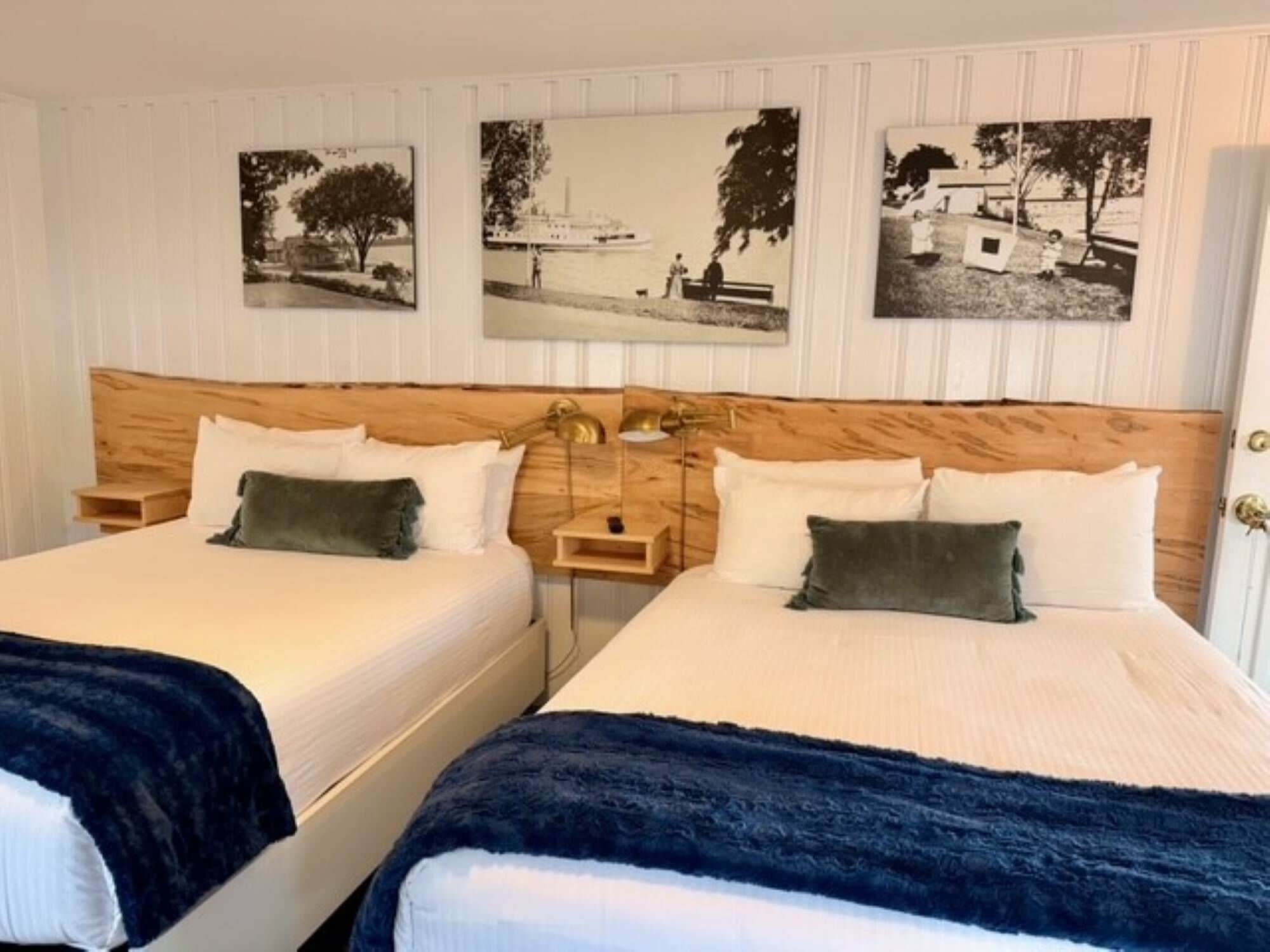Habitación doble con dos camas, cabecero de madera, mesitas de noche y tres fotografías blanco y negro en la pared.