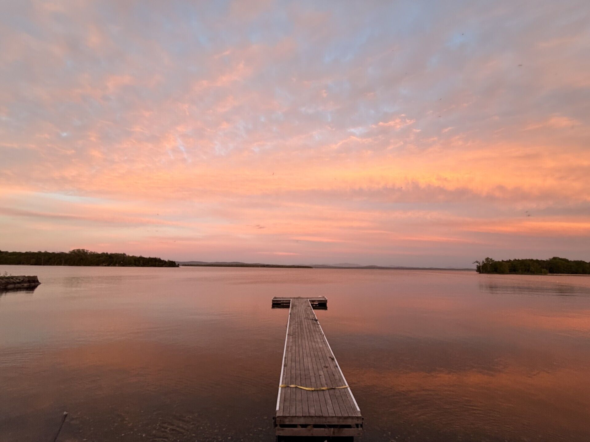 Une jetée en bois s’étendant sur une étendue d’eau calme, avec un ciel au coucher du soleil.