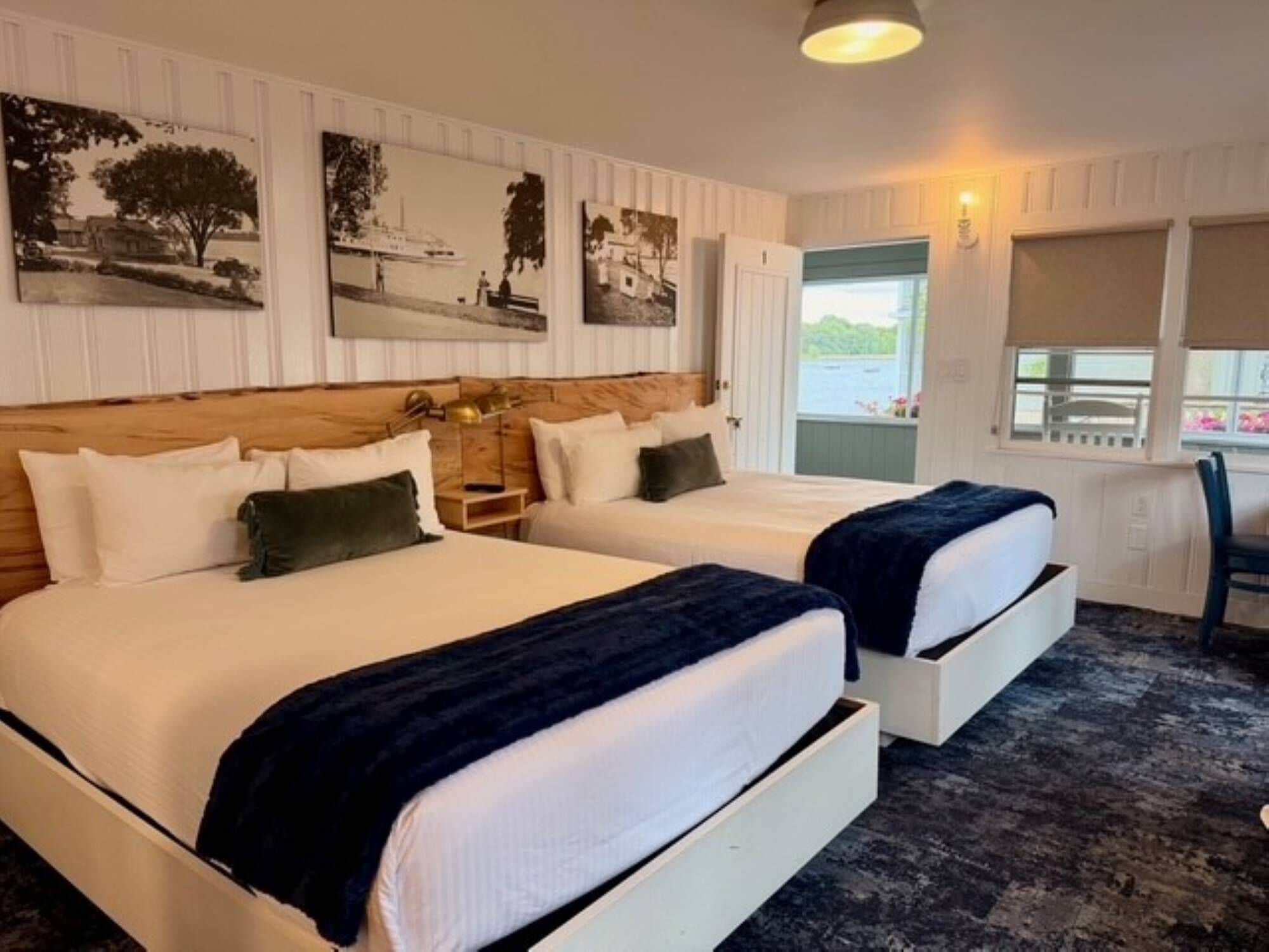 A hotel room with two beds, a wooden headboard, a nightstand, and a window with a view.