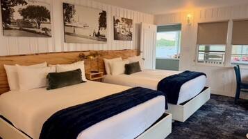 A hotel room with two beds, a wooden headboard, a nightstand, and a window with a view.
