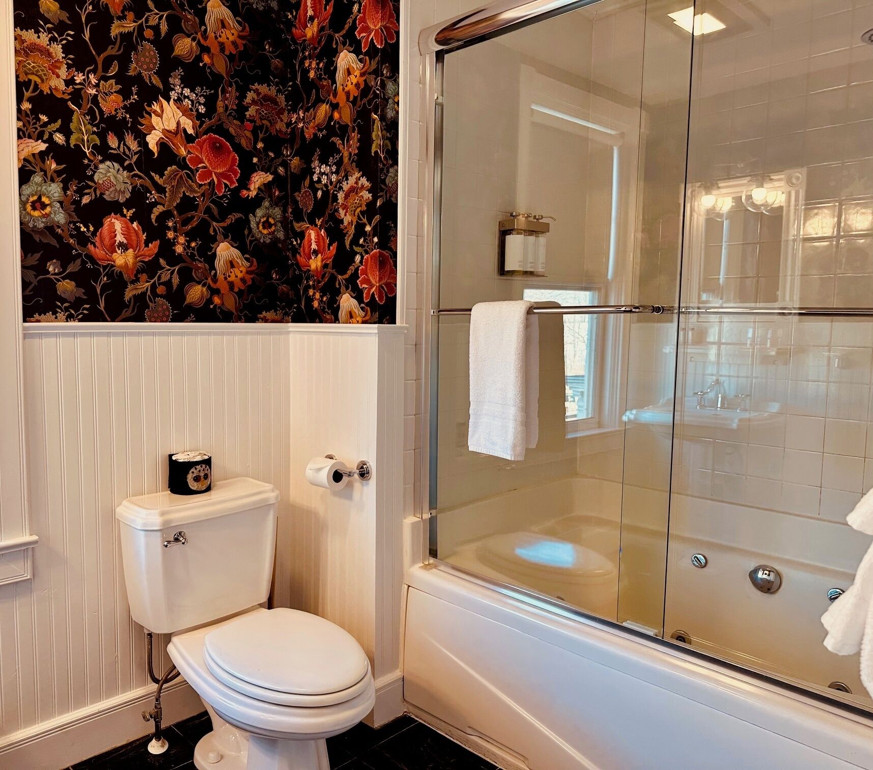 A bathroom with a toilet, a glass shower enclosure, and a floral wallpaper design.