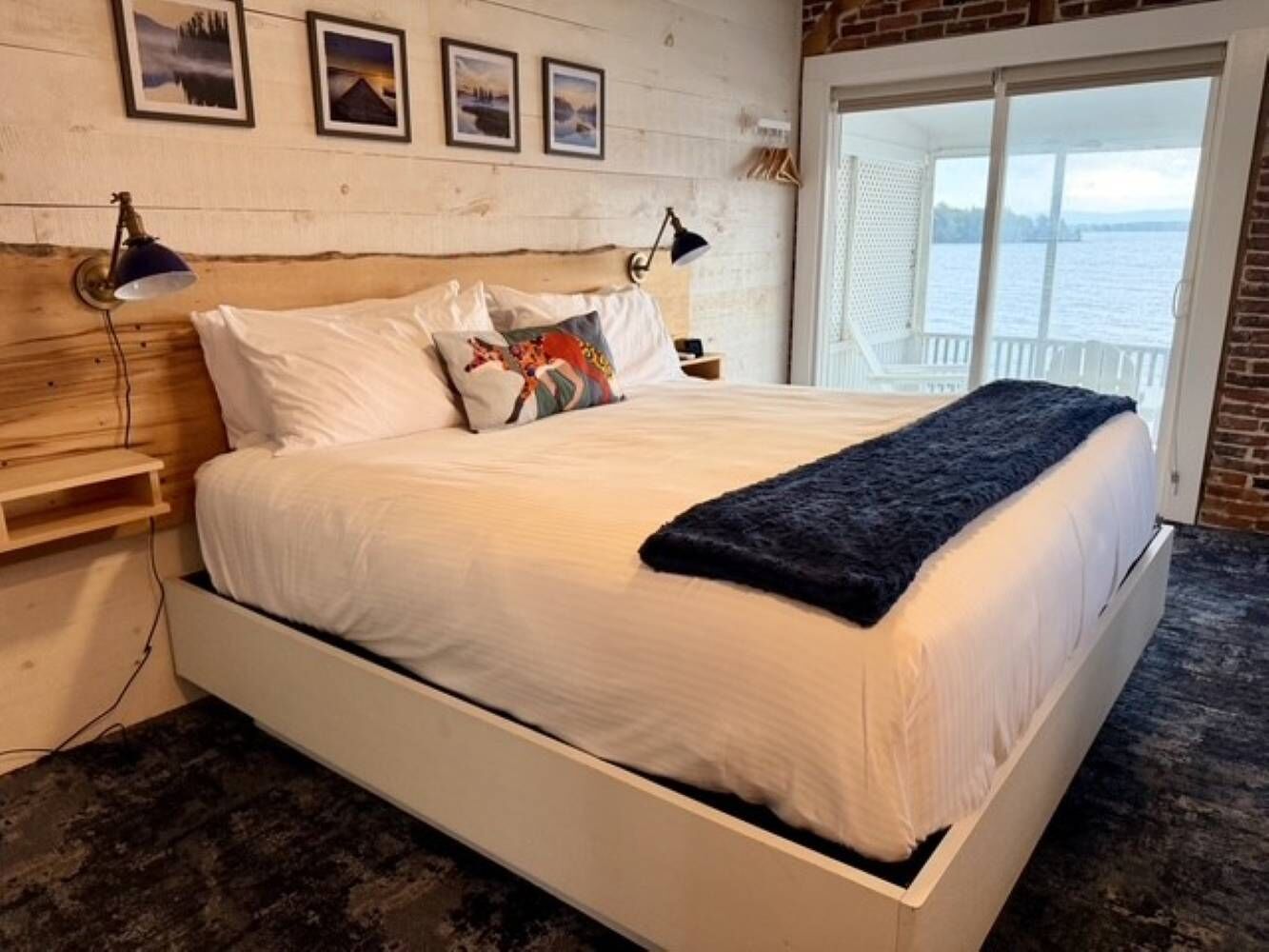 Uma cama com roupa de cama branca, um cobertor escuro e uma cabeceira de madeira.