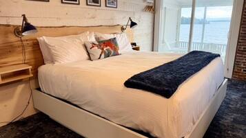 Uma cama com roupa de cama branca, um cobertor escuro e uma cabeceira de madeira.