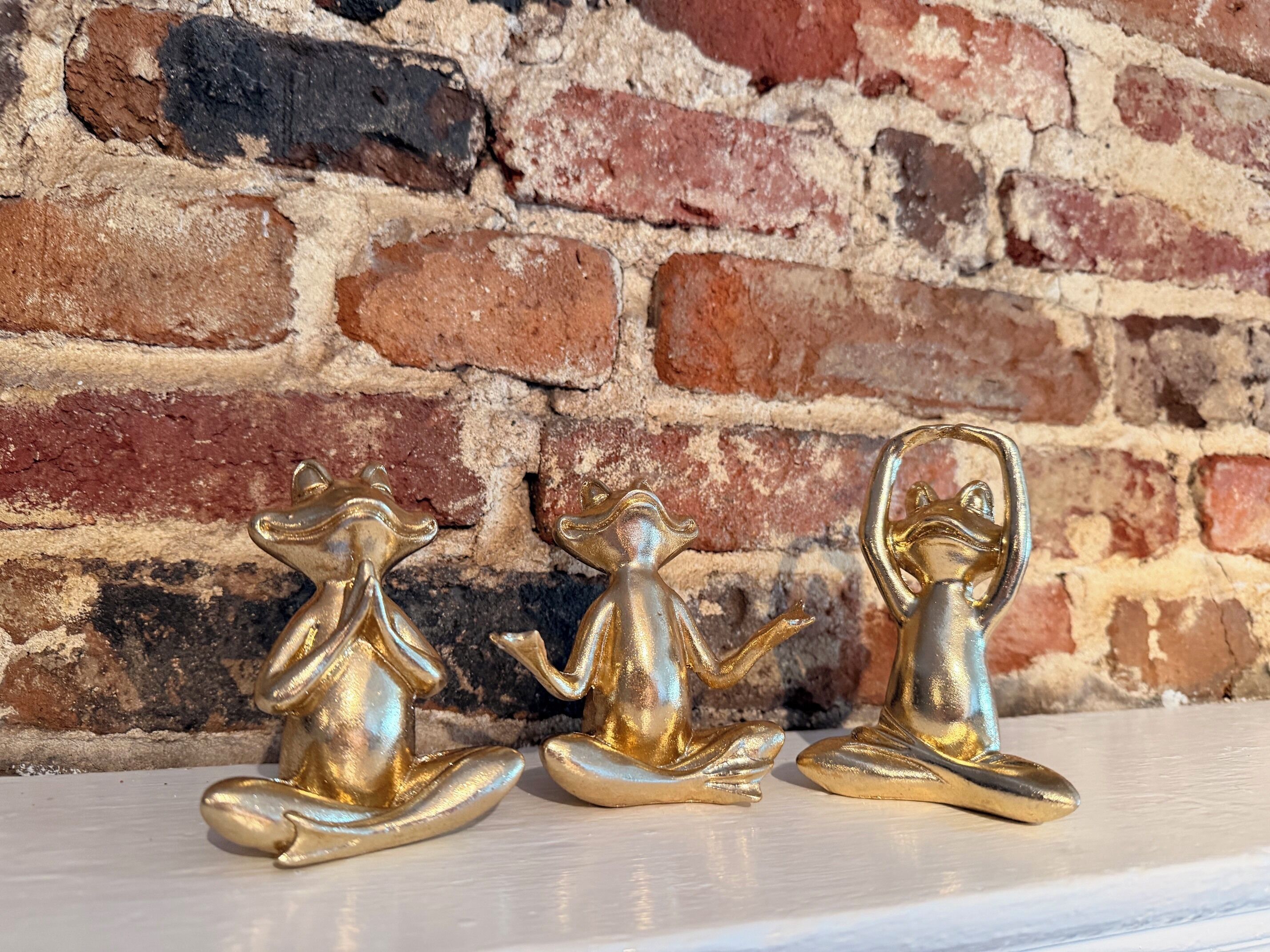 Drie gouden Boeddhabeelden op een wit oppervlak voor een bakstenen muur.