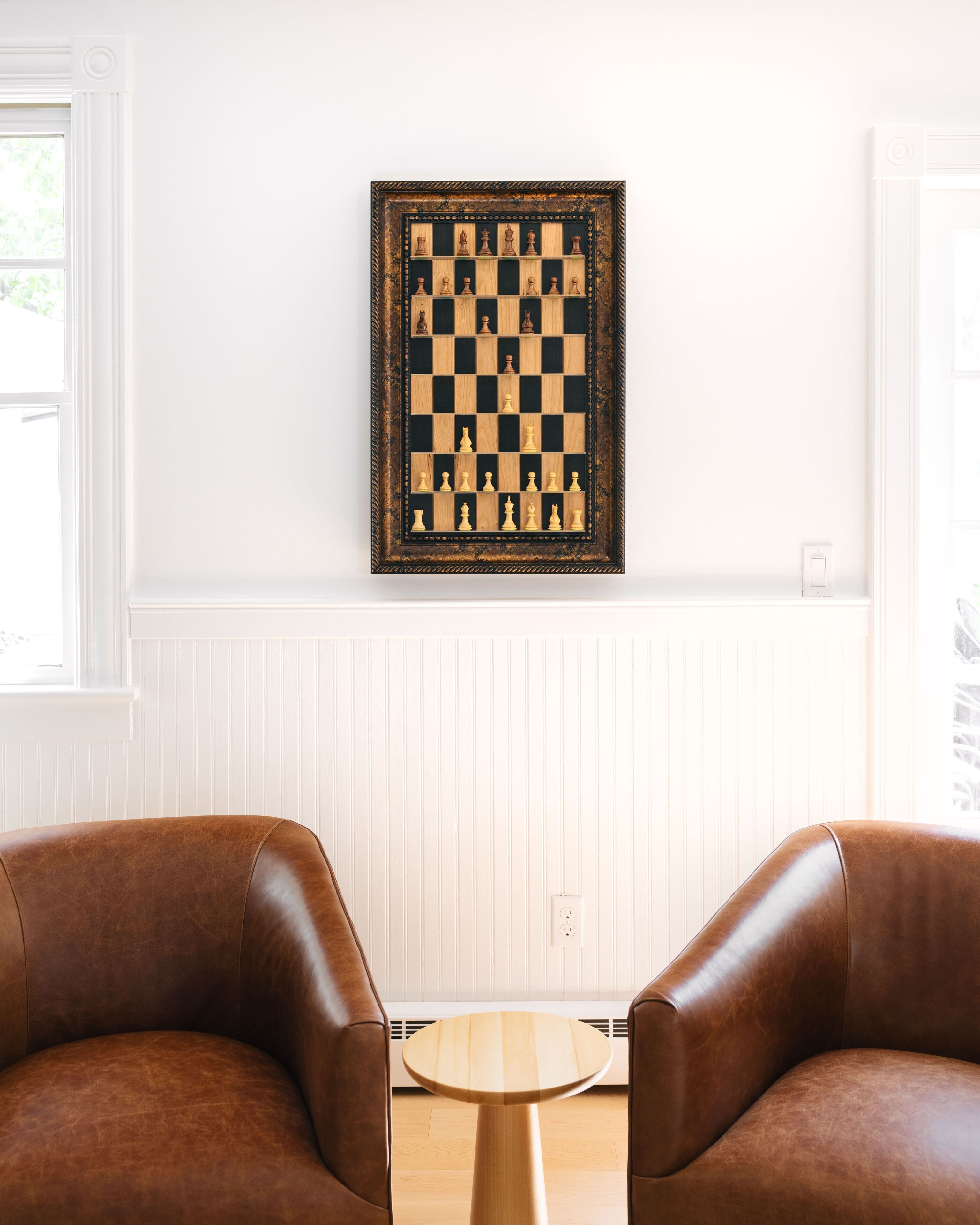 Una habitación con un tablero de ajedrez en la pared, dos sillones de cuero y una pequeña mesa de madera.