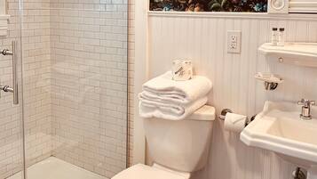 A bathroom with a white toilet, a shower enclosure, a sink, and a decorative floral wallpaper.