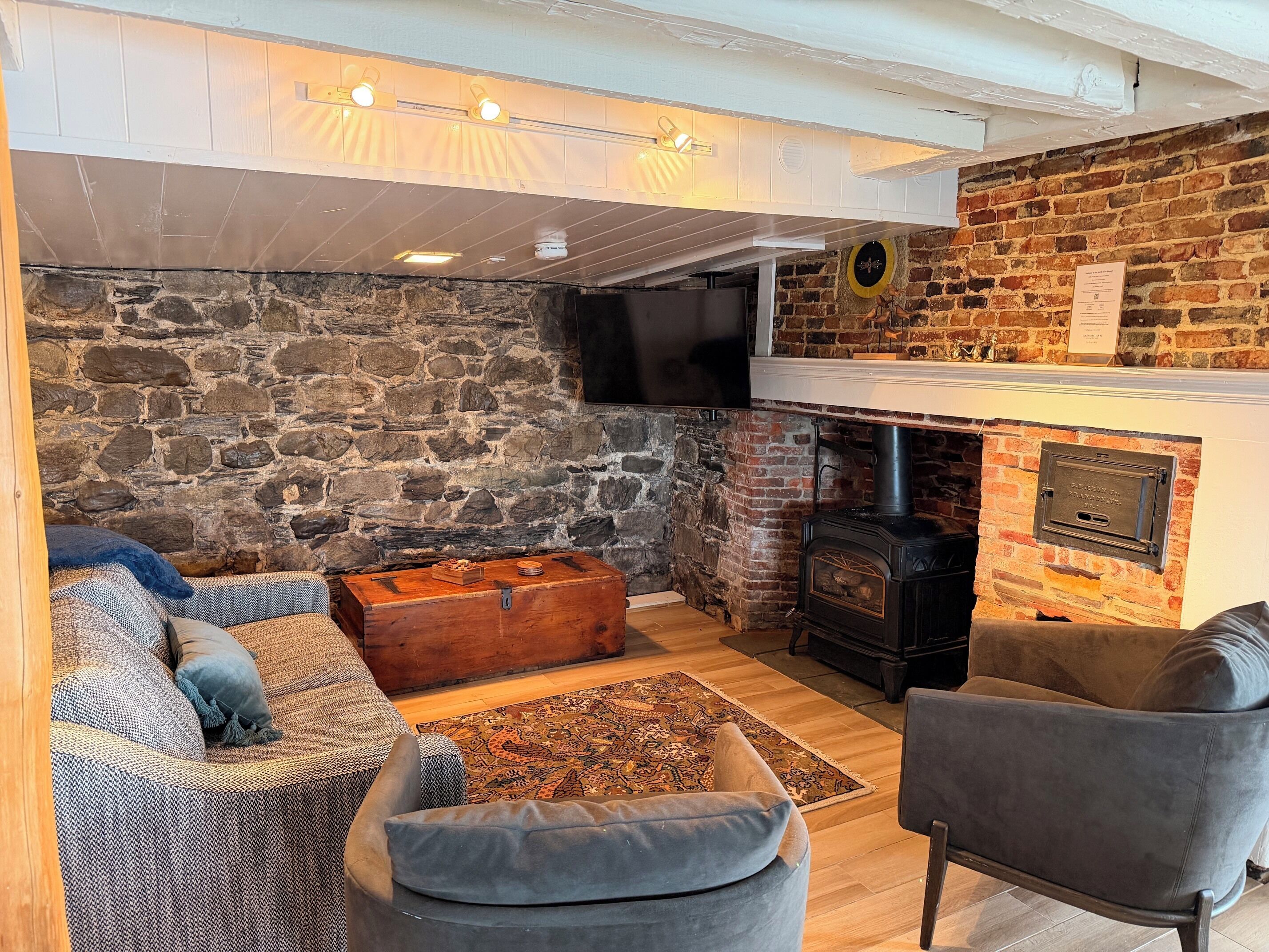 Ein gemütliches Wohnzimmer mit Steinwand, Kamin, Fernseher und bequemen Sitzgelegenheiten.