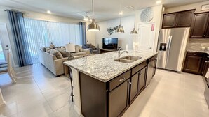 Una cocina moderna con una isla grande, muebles oscuros, electrodomésticos de acero inoxidable e iluminación colgante.