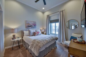 Quarto com cama, mesa de cabeceira, luminária, cadeira e janela com cortinas.