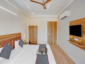 A hotel room with a bed, a ceiling fan, a TV mounted on the wall, and a wardrobe.