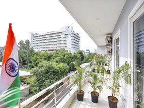 Een balkon met bloempotten, een vlag en uitzicht op een meerhoog gebouw.